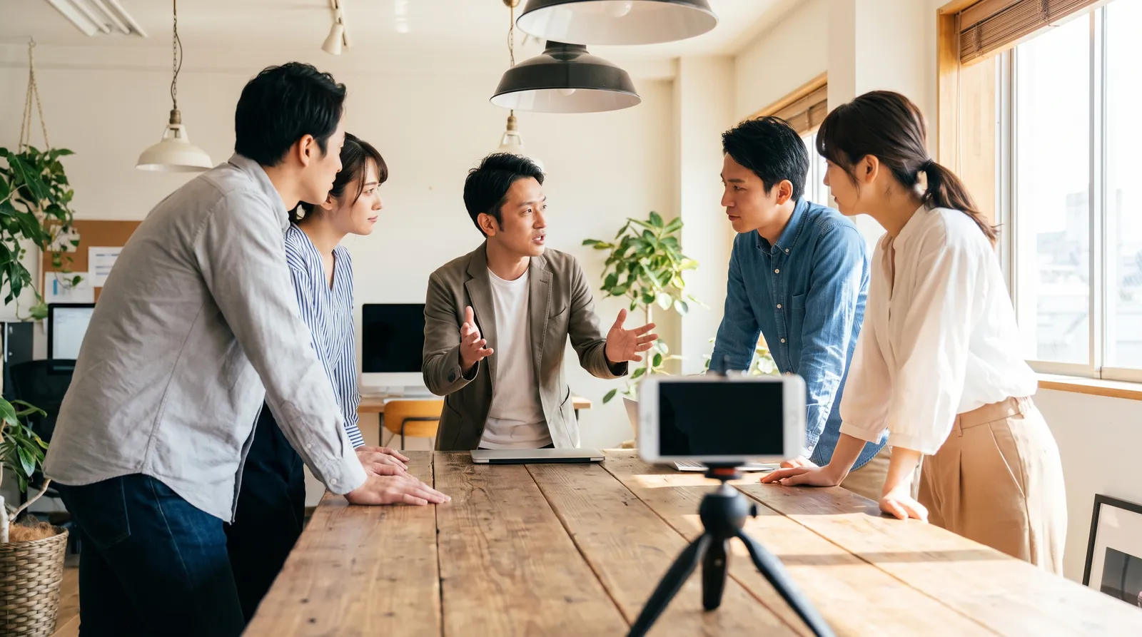 Small startup team gathered around a table while a colleague speaks to a phone on a tripod