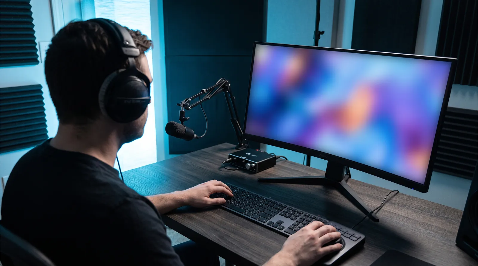 Editor in headphones working at a desk with microphone and controller, monitor angled away and blurred